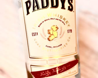 May include: A clear glass bottle with a white label that reads "Paddy's Irish Whiskey, Blend of Grain, Malt and Pot Still, Est! Cork, Ireland, 1779, Cork Distilleries Co.". The bottle is filled with a white candle and has a red label that reads "Paddy Flaherty" on the bottom.