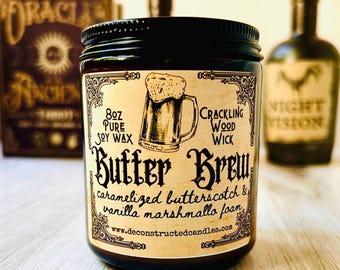 May include: A glass jar candle with a black lid and a label that reads "Butter Brew." The label features a beer mug illustration and the text "caramelized butterscotch & vanilla marshmallow foam." The candle is 8 oz and made with pure soy wax.