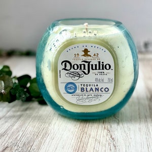 May include: A blue glass candle jar with a white label that reads "Don Julio Tequila Reserva de 1942 100% de Agave Tequila Blanco 40% alc./vol. 750 ml. Atotonilco el Alto, Jalisco, Mexico."
