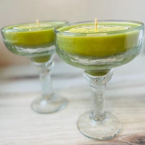 May include: Two green glass margarita glasses with candles inside. The candles are green and have a white label that says "Margarita Time".