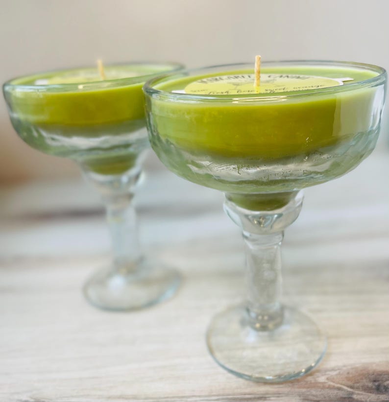 May include: Two green glass margarita glasses with candles inside. The candles are green and have a white label that says "Margarita Time".