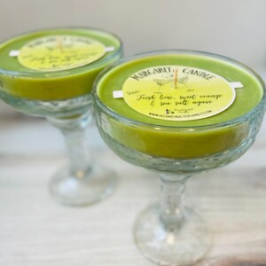 May include: Two green margarita candle jars in the shape of a margarita glass. The candles have a white label that reads "Margarita Candle" and "Fresh lime, sweet orange & sea salt agave".
