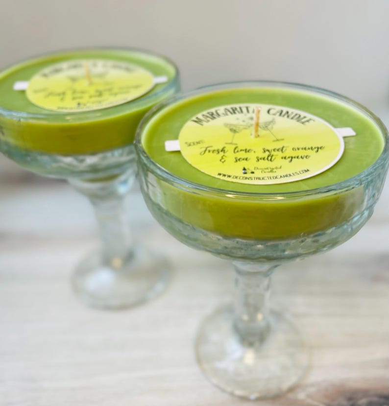 May include: Two green margarita candle jars in the shape of a margarita glass. The candles have a white label that reads "Margarita Candle" and "Fresh lime, sweet orange & sea salt agave".