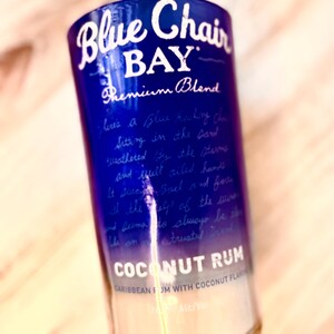 May include: A glass bottle with a blue and white label that reads "Blue Chair Bay Premium Blend Coconut Rum Caribbean Rum with Coconut Flavor 2% Alc/Vol".