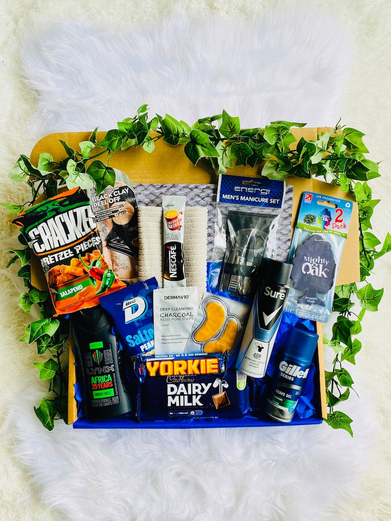 Puede incluir: Una caja de regalo azul llena de varios art&iacute;culos, que incluyen una barra de chocolate, una botella de spray corporal, un paquete de pretzels, una mascarilla facial, un paquete de tiras para poros nasales, un juego de manicura para hombres, una pastilla de jab&oacute;n y un tubo de gel de afeitar.