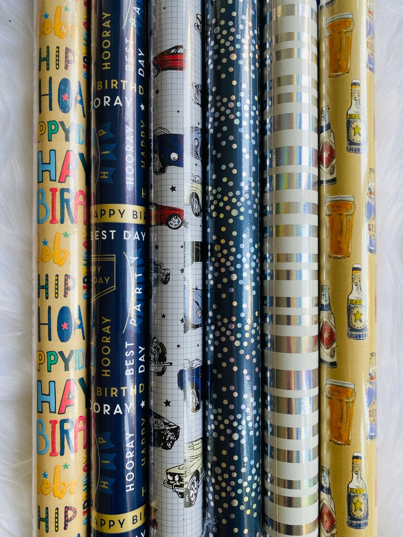 Puede incluir: Cuatro rollos de papel de regalo con diferentes dise&ntilde;os. El primer rollo tiene un fondo amarillo con texto colorido que dice "Hip Hooray Happy Birthday Best Day Party". El segundo rollo tiene un fondo azul con estrellas blancas y un patr&oacute;n de cuadr&iacute;cula. El tercer rollo tiene un patr&oacute;n de rayas plateadas y blancas. El cuarto rollo tiene un fondo amarillo con un dise&ntilde;o de botella de cerveza marr&oacute;n y vaso.