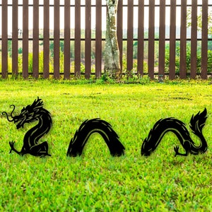Puede incluir: Una escultura de jardín de dragón de metal negro que consta de tres piezas separadas. La primera pieza presenta la cabeza y el torso delantero del dragón, mientras que las otras dos piezas representan las secciones curvas del cuerpo.