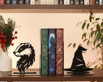 May include: A pair of black metal bookends featuring a badger silhouette on the left and a pointed wizard hat silhouette on the right, supporting three hardcover books with green, blue, and red decorative spines on a wooden shelf.