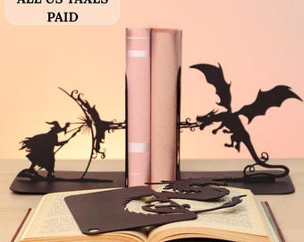 May include: A set of black metal bookends featuring a silhouette of a wizard casting a spell at a dragon, with a matching black metal dragon bookmark resting on an open book. The text ALL US TAXES PAID is visible in a light-colored rounded box.