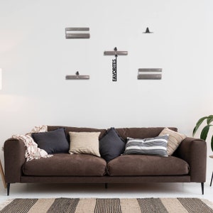 Pu&ograve; includere: Un set da parete composto da quattro mensole rettangolari in metallo con texture a coste e un cartello centrale verticale in metallo nero con una freccia rivolta verso l'alto e la parola FAVORITES in grassetto maiuscolo.