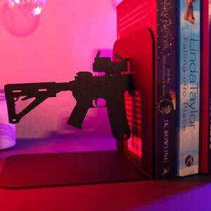 May include: Black metal bookends shaped like a rifle with a scope. The bookends are holding up three books, one by J.K. Rowling, one by Mary Parker, and one by Linda Taylor.
