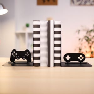 May include: Black metal bookends shaped like a video game controller. The bookends are holding up three books with black and white stripes.