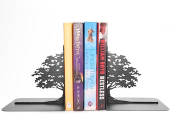 May include: A pair of black metal bookends featuring a silhouette of a tree with spreading branches and a flat base. The bookends are positioned on either side of four books, including titles by J.K. Rowling, Linda Taylor, and William Boyd.