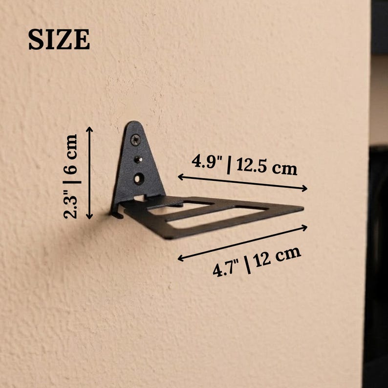 Pu&ograve; includere: Una staffa per mensola da parete in metallo nero con base triangolare e braccio di supporto piatto. La staffa presenta dimensioni di 6 cm di altezza, 12,5 cm di profondit&agrave; e 12 cm di larghezza, come indicato dalle etichette nell'immagine.