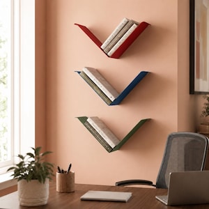 Peut inclure: Trois étagères murales en forme de V, de couleurs rouge, bleue et verte, contenant chacune une petite pile de livres. Les étagères sont disposées verticalement sur un mur couleur pêche, offrant une solution de rangement pour les livres.