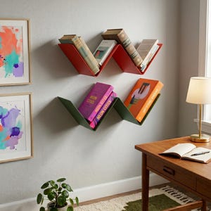 Op de afbeelding: Twee W-vormige wandplanken, één rood en één groen, elk met verschillende boeken. De rode plank bevat drie boeken, terwijl de groene plank twee boeken bevat, waaronder een boek met de titel Neon Cities en een met een grafische kaft.