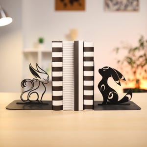 May include: Black metal bookends featuring a stylized silhouette of a fox and a wolf. The bookends are on a wooden surface with a set of books in the background.