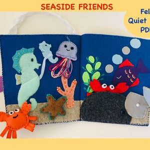 May include: A felt quiet book with a blue background featuring a seahorse, jellyfish, crab, starfish, coral, seaweed, fish, and a clam. The book has a handle and is titled "Seashore Friends Felt Quiet Book PDF".