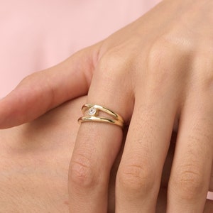 May include: A gold ring with a single clear stone set in the center. The ring is worn on the ring finger of a hand with white nail polish.