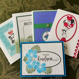 May include: Five handmade greeting cards with different designs. The cards are all white with colorful accents. One card features a panda bear, another has a jar with a grasshopper, another has a girl holding balloons, another has a floral design, and the last one has a happy birthday message.