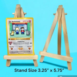 May include: A yellow and white card with a pixelated image of two people and two cats. The card is titled "The Anniversary 2022 HP" and has the text "I Choose You!" and "Happy anniversary to my better half! I choose you today, tomorrow, and always!" The card is displayed on a small wooden easel that measures 3.25 inches by 5.75 inches.