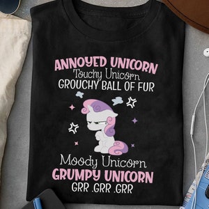 May include: Black t-shirt with a pink and purple cartoon unicorn with a grumpy expression. The text reads "Annoyed Unicorn Touchy Unicorn Grouchy Ball of Fur Moody Unicorn Grumpy Unicorn GRR.GRR.GRR"