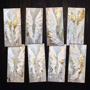 May include: Eight abstract paintings of white angel wings with gold accents on a dark wood background.