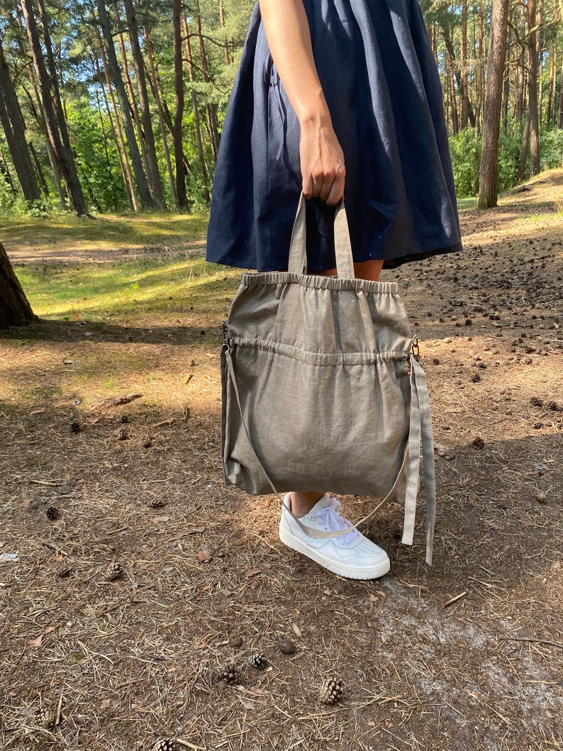 Natural linen color linen tote bag. Handmade from waxed linen. The bag is rectangular shape with short handles and shoulder strap, has inside pocket for phone and wallet. The tote bag closes with side straps. The shoulder strap is attached with darkened metal details and can be attached or removed.