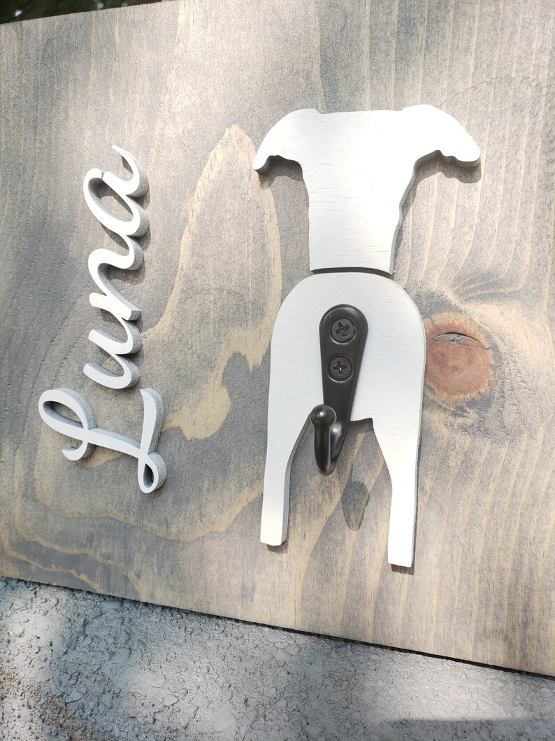 May include: White wooden dog-shaped coat hook with the name "Luna" written in white on a gray wooden background.