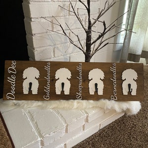 May include: A wooden coat rack with five white dog silhouettes, each with a black hook. The silhouettes are labeled "Doodle Dee", "Goldendoodles", "Sheepadoodles", and "Bernedoodles".