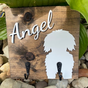 May include: Wooden dog leash holder with two hooks. The holder is painted brown and has a white silhouette of a dog with the name "Angel" written in white cursive letters.