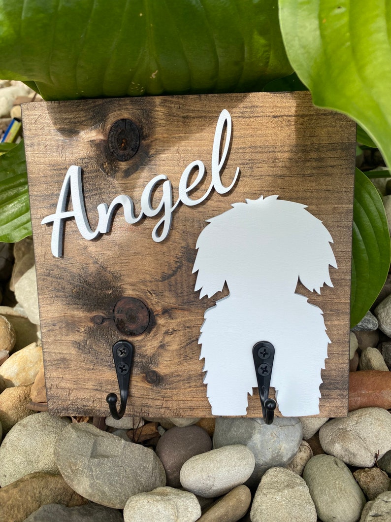 May include: Wooden dog leash holder with two hooks. The holder is painted brown and has a white silhouette of a dog with the name "Angel" written in white cursive letters.
