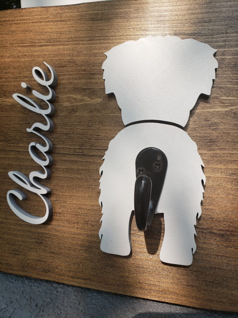 May include: Wooden sign with a white silhouette of a dog's rear end with a black hook attached. The name "Charlie" is written in white on the left side of the sign.