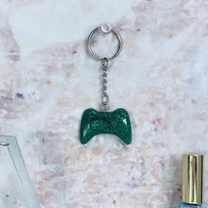 May include: A green glitter resin game controller keychain with a silver chain and ring.