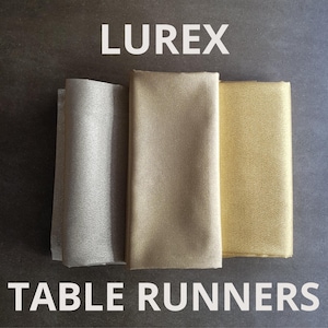 Könnte beinhalten: Drei Tischläufer aus Lurex-Gewebe. Die Läufer sind silber, gold und hellgold.