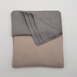 Puede incluir: Un juego de sábanas de lino gris y beige. Las sábanas están dobladas y apiladas una encima de la otra.