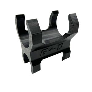 Może przedstawiać: Czarny wspornik drukowany w 3D z zakrzywioną g&oacute;rą i czterema nogami. Na wsporniku wygrawerowano litery "G < P". Wspornik jest przeznaczony do trzymania przedmiotu.