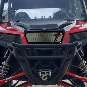 May include: A red off-road vehicle with a black mesh grille and a red "6.0" emblem. The vehicle has a black bumper and a silver tow hook.