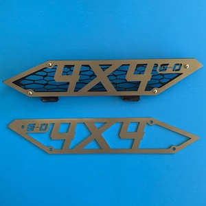 May include: Two metal 4x4 grill inserts. The top insert has a black mesh grille and the bottom insert is open. Both inserts have the text "G-O" and "4x4" cut out.
