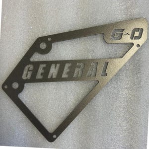 May include: A metal sign with the words "GENERAL" and "G-O" cut out. The sign is a dark gray color and has a textured finish.