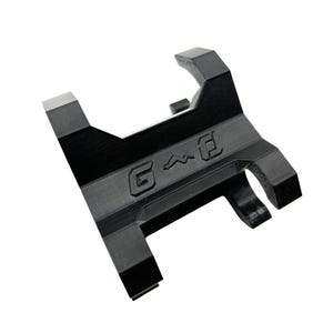 Może przedstawiać: Czarny, kątowy metalowy przedmiot z wytłoczonymi literami "G^D". Obiekt ma prostokątną podstawę z karbowaną krawędzią i dwoma zakrzywionymi ramionami rozciągającymi się ku g&oacute;rze. Og&oacute;lny projekt jest geometryczny i przemysłowy.