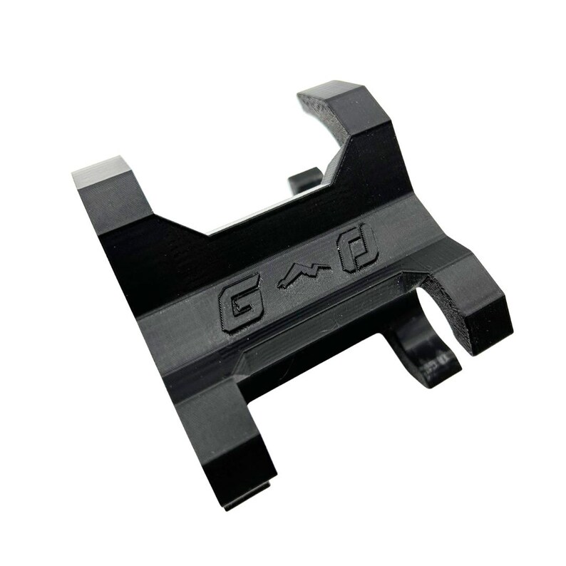 Może przedstawiać: Czarny, kątowy metalowy przedmiot z wytłoczonymi literami "G^D". Obiekt ma prostokątną podstawę z karbowaną krawędzią i dwoma zakrzywionymi ramionami rozciągającymi się ku g&oacute;rze. Og&oacute;lny projekt jest geometryczny i przemysłowy.