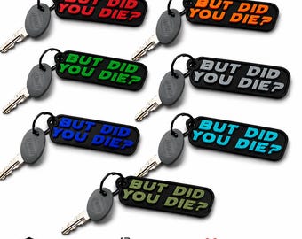 May include: Seven rectangular black keychains, each attached to a grey Bauer key, featuring the embossed text BUT DID YOU DIE? in various colors including red, orange, green, grey, blue, light blue, and olive green, arranged in a grid pattern.