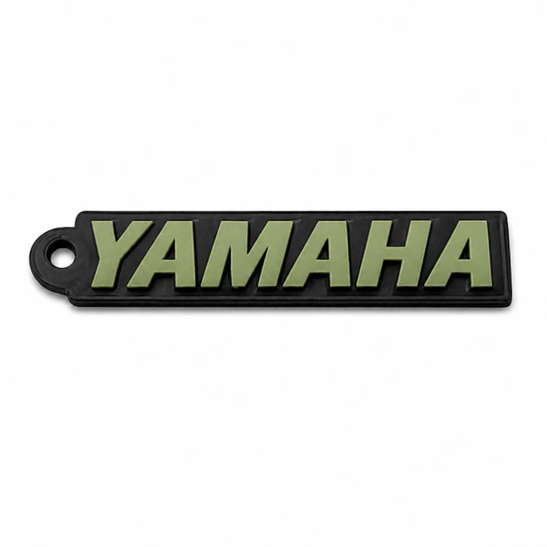 Pu&ograve; includere: Un portachiavi rettangolare nero con la scritta "YAMAHA" in lettere verde oliva. Il portachiavi ha un piccolo foro circolare sul lato sinistro.