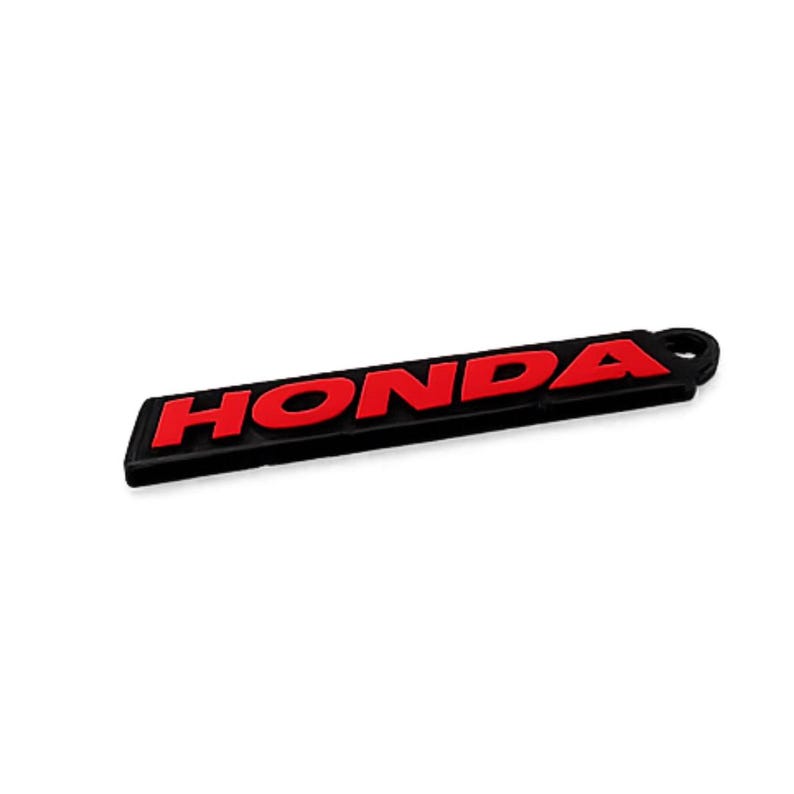 May include: Black and red Honda keychain. The word "HONDA" is in red, bold letters on a black rectangular background. The keychain has a small loop on one end.