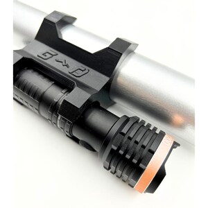 Może przedstawiać: Czarna latarka z żebrowaną głowicą i pomarańczowym akcentem, zamontowana na srebrnym cylindrycznym obiekcie. Uchwyt jest czarny i zawiera litery "G" i "P". Latarka jest przeznaczona do użytku taktycznego lub zewnętrznego.