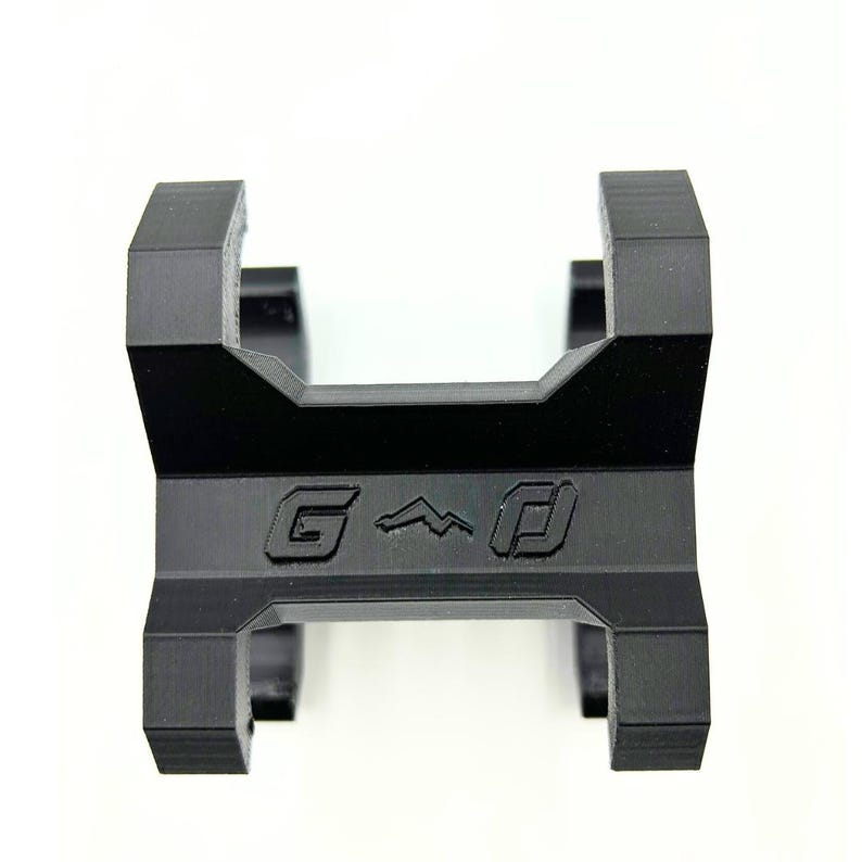 Może przedstawiać: Czarny, geometryczny wspornik z literami "G" i "D" oraz grafiką g&oacute;r. Wspornik ma prostokątny kształt z serią pionowych i poziomych podp&oacute;r. Obiekt wykonany jest z matowego czarnego materiału i umieszczony na białym tle.