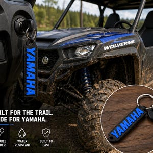 Pu&ograve; includere: Portachiavi Yamaha nero e blu con la scritta "YAMAHA" in blu. Il portachiavi &egrave; attaccato a una chiave nell'accensione di un ATV Yamaha Wolverine. &Egrave; visibile anche il testo "BUILT FOR THE TRAIL. MADE FOR YAMAHA.".