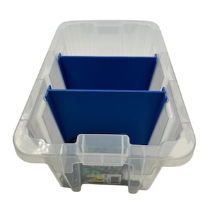 May include: A clear plastic storage bin with a blue divider. The bin has a rectangular shape with rounded corners and a handle on the front. The blue divider creates two compartments inside the bin.