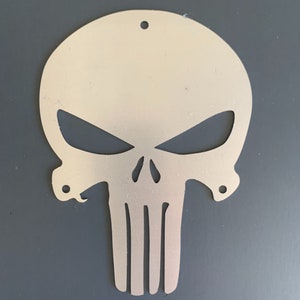 May include: A silver metal cutout of the Punisher skull, a popular comic book character. The skull is detailed with a menacing expression and a distinctive lower jaw.